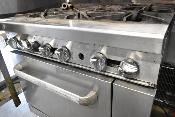 Stainless steel 6-burner commercial gas range with oven, over shelf, back splash, knobs, and commercial casters shown, used condition.