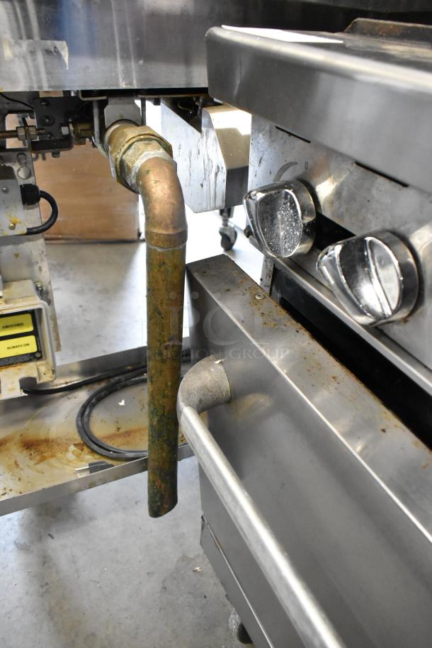 Stainless steel commercial gas range with 6 burners, oven, over shelf, backsplash, and commercial casters. Visible wear.