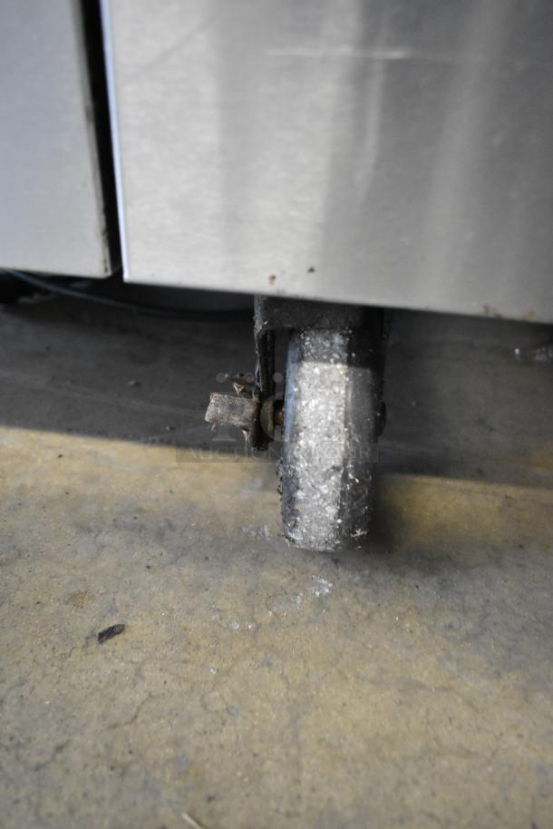 Stainless steel commercial range with gas-powered 6 burners, oven, over shelf, and back splash on commercial casters.