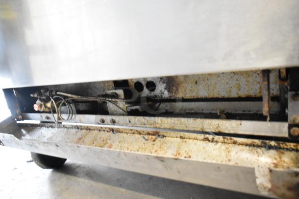 Stainless steel commercial gas burner range base, showing signs of use with visible grease and rust, mounted on casters.