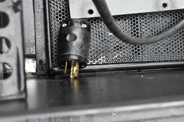 Metal commercial merchandiser plug detail, 208/230 volts, 1 phase. Black and gold connector, perforated metal background.