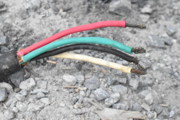 Electrical wires exposed on rocky ground, featuring red, black, green, and yellow wires.