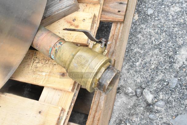 Stainless steel bagel kettle spout with brass valve marked "400 WOG," mounted on a wooden pallet. Slight wear visible.