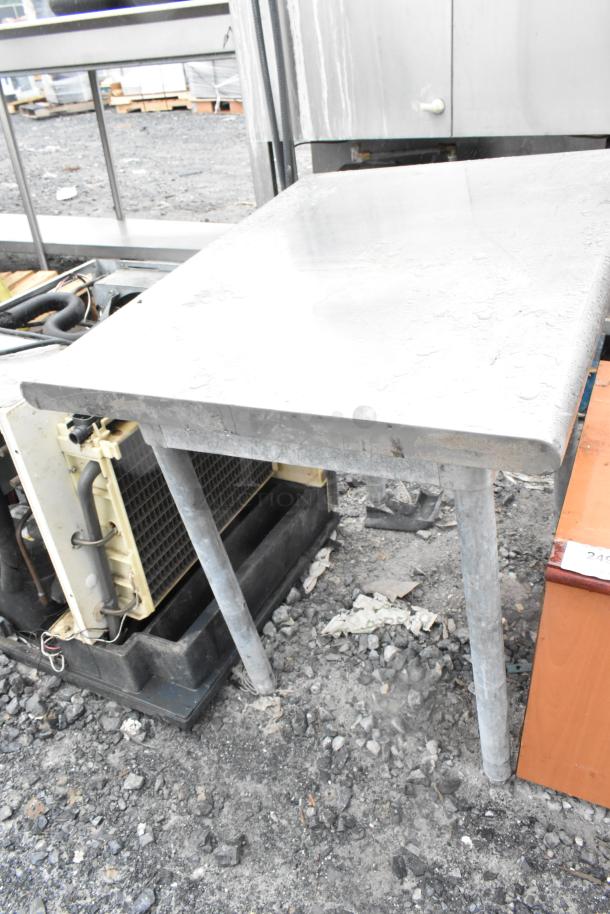 Stainless steel table, rectangular, sturdy legs, scratched surface, outdoor setting, suitable for industrial use.
