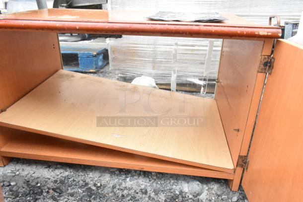 Wood pattern 2-door cabinet, showing significant wear with a tilted shelf and chipped edges. No visible labels or markings.
