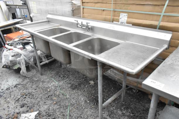 Stainless Steel 3 Bay Sink with dual drain boards and handles. Includes faucet, slightly worn condition, ideal for commercial use.