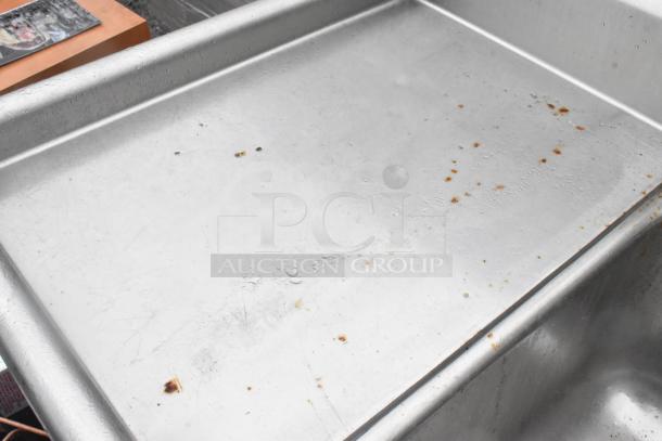 Stainless steel 3-bay sink with dual drain boards and handles, showing surface wear and marks. Ideal for commercial use.