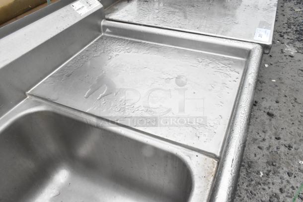 Stainless steel 3-bay sink with dual drain boards and handles, in good condition, showing water droplets on surface.