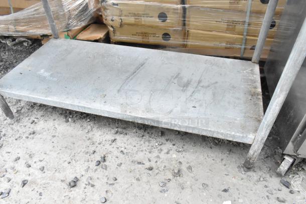 Stainless steel table with metal under shelf, visible scratches, includes metal baskets; suitable for industrial use.