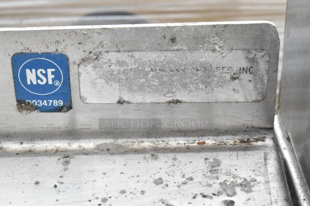 Stainless steel table with metal under shelf, visible NSF label indicating certified standards. Contains metal baskets. Signs of wear present.