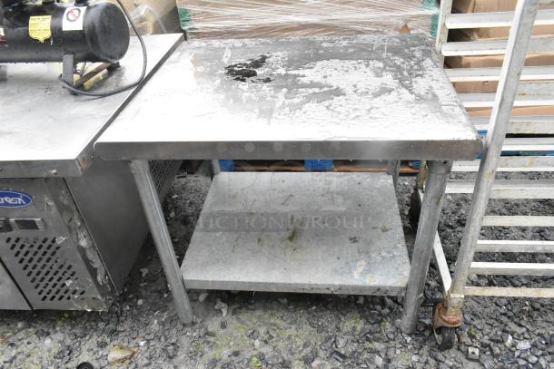 Stainless steel table with metal under shelf, wet surface, industrial use, scratches and marks indicating wear.