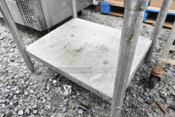 Stainless steel table with a metal under shelf, showing signs of wear and rust on legs. Suitable for industrial use.
