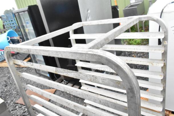 Metal commercial transport pan rack on casters, showing some wear and outdoor exposure. Sturdy metal construction.