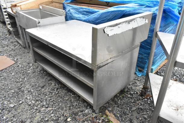 Stainless steel equipment stand with two under shelves, shows signs of wear. Ideal for kitchen or industrial use.