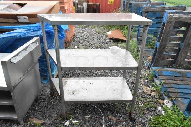 Stainless steel 3-tier shelving unit on commercial casters, showing minor wear, ideal for storage or commercial use.