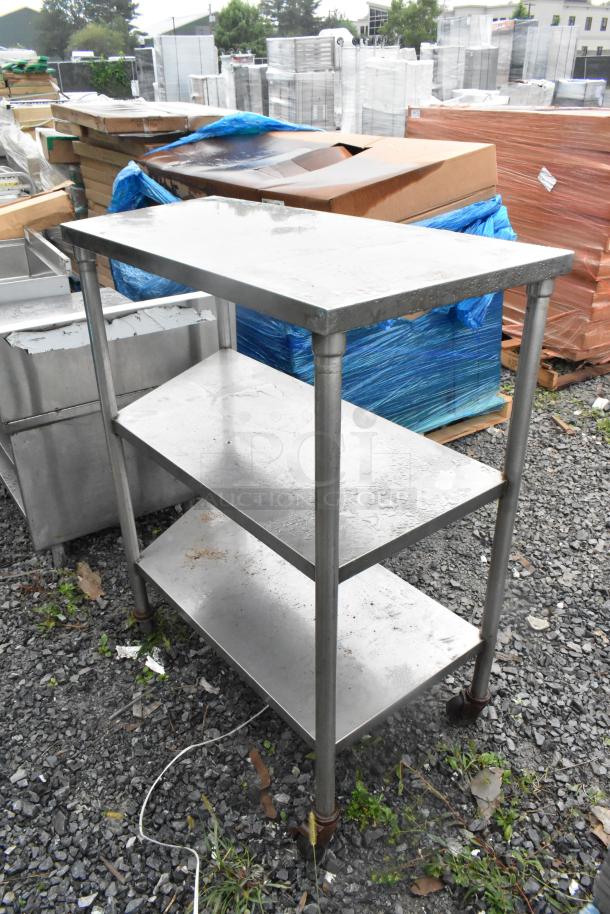 Stainless steel 3-tier shelving unit with commercial casters, showing wear, suitable for industrial use.