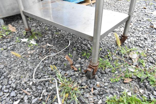 Stainless steel 3-tier shelving unit with commercial casters. Features a sturdy frame and wheels for mobility. Slight rust visible on casters.