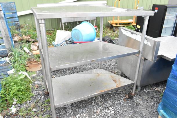 Stainless steel 3 tier shelving unit on commercial casters, rust visible, outdoor setting, ideal for commercial storage.