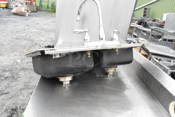 Metal 2 bay sink with faucet and handles, stainless steel, used condition, visible rust on edges, suitable for commercial use.