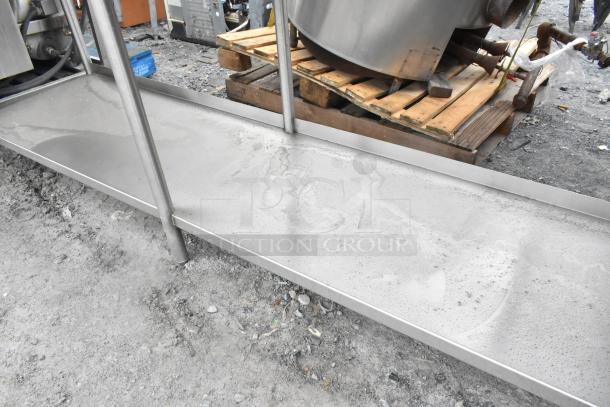 Stainless steel table with under shelf and back splash, showing surface wear, sturdy legs, suitable for industrial use.