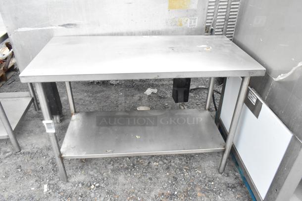 Stainless steel table with under shelf, industrial-grade, used condition with some surface wear, sturdy metal legs.