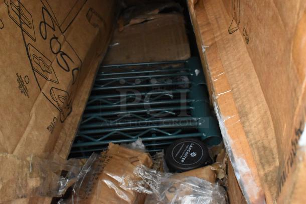 Box with assorted new items including stanchion parts, shelves, and wall racks; some packaging is torn. Lancaster branding visible.