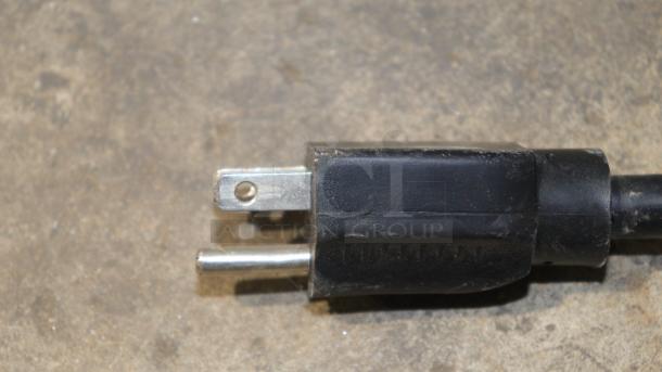 Close-up of a black electrical plug with two metal prongs on a textured surface.