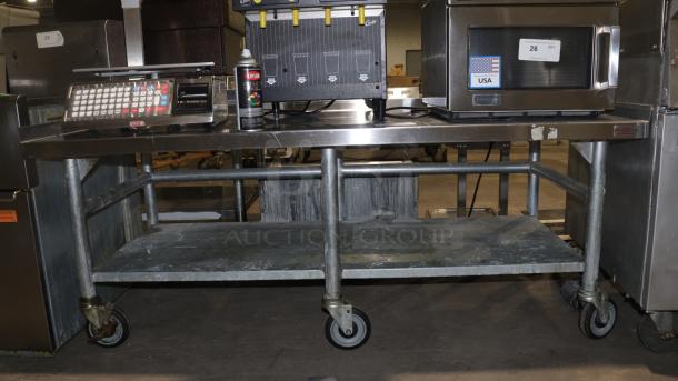 61" stainless-steel counter with caster wheels, used for baking or storage. Features worn top surface, robust frame.