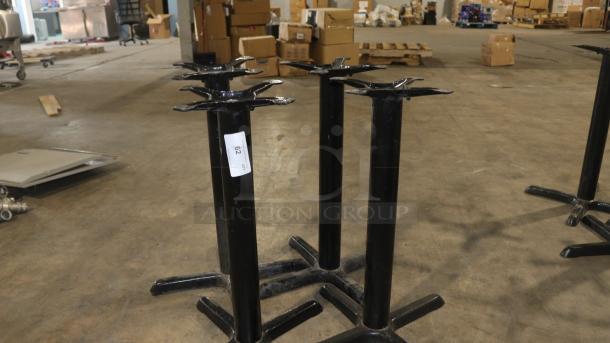 Black FLAT Tech KX22 22" x 22" self-stabilizing table bases, model CT2007, shown in a warehouse. Label visible on one base.