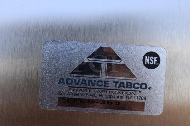 Close-up of the Advance Tabco TFLG-365 model label on a stainless steel commercial work table.