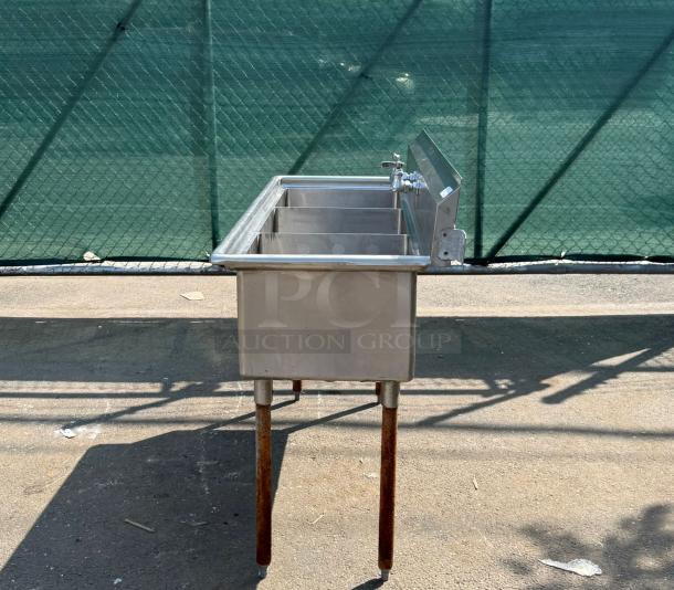 Stainless steel triple sink with three basins, side faucet, and rusted metal legs, suitable for commercial use.