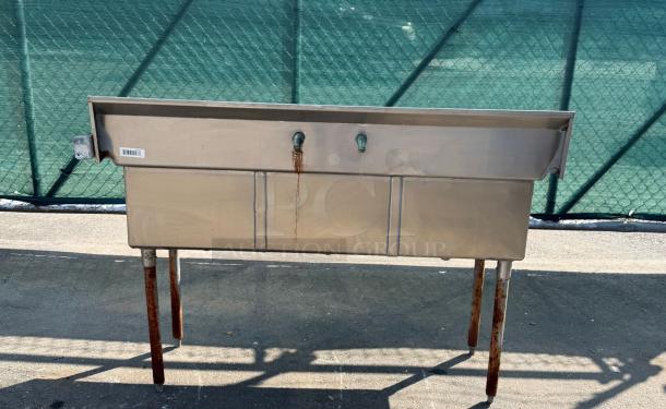 Stainless Steel Triple Sink with two faucets, rust marks, and a barcode label on the side. Sturdy, industrial use.