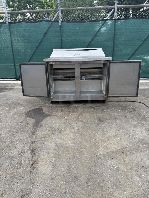 Kelvinator KCHMT48.18 48" Mega Top Sandwich/Salad Prep Table, refrigerated base, two doors open, outdoor setting.