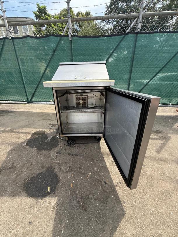 TRUE TSSU-27-12M refrigerated sandwich prep table, open door, visible interior shelves, outdoor setting.