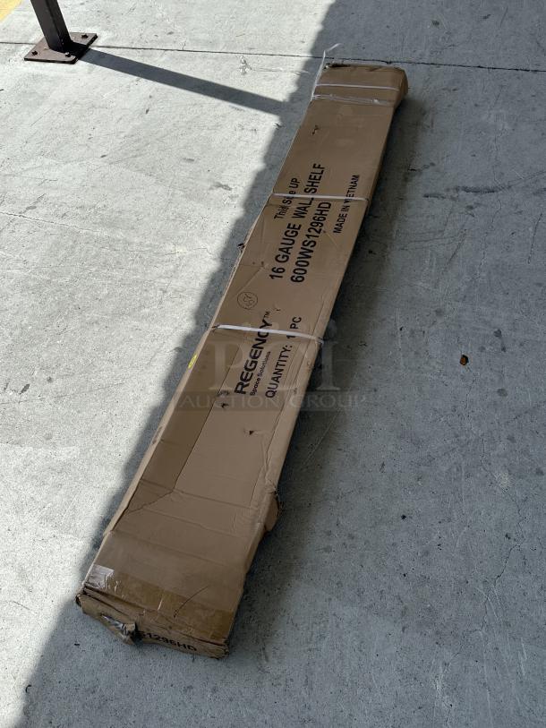 Regency stainless steel 12" x 96" wall shelf in original packaging, minor dents visible. Model 600WS1296HD, made in Vietnam.