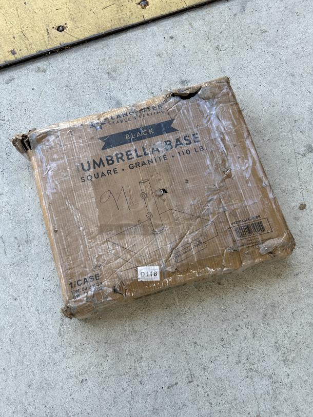 Brand new Lancaster Table & Seating black granite umbrella base, model 427BASEGRNBK, 110 lb., box with visible wear.