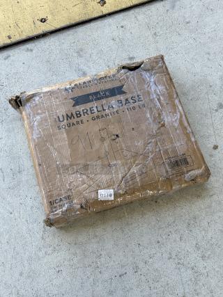 Brand new Lancaster Table & Seating black granite umbrella base, model 427BASEGRNBK, 110 lb., box with visible wear.