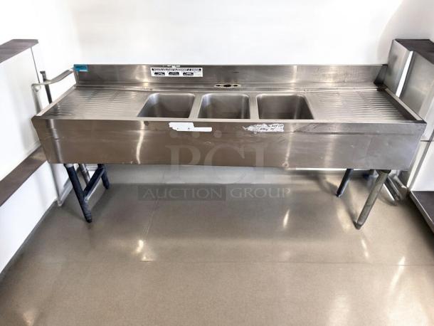 Three-compartment stainless steel bar sink with dual drainboards, 72"x24"x35", excellent condition, fully tested, visible labels.