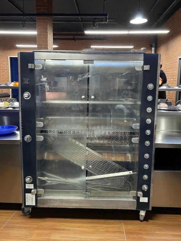 Commercial rotisserie oven in stainless steel, large glass doors, multiple knobs for settings, on wheels, good condition.