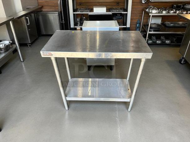 Stainless steel worktop table with shelf, excellent condition, sturdy cylindrical legs, ideal for kitchens or workshops.