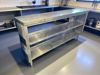 Stainless steel custom-made table with two shelves, sturdy construction, minor surface wear, ideal for kitchen use.