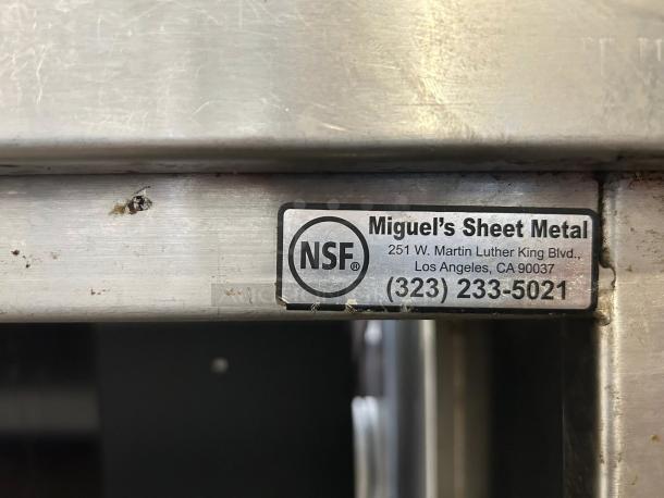 Stainless steel custom-made table by Miguel's Sheet Metal, NSF certified, sturdy, some surface wear, contact info visible.