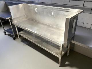 All stainless steel custom-made table with two electrical outlets, featuring a backsplash and lower shelf. Excellent condition.