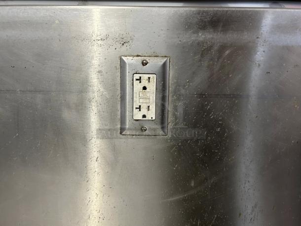 Stainless steel custom-made table with two power outlets, showing minor surface scratches.