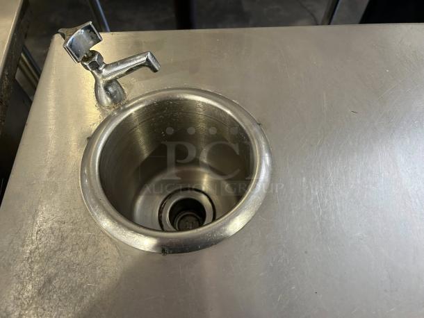 Stainless steel custom-made table with integrated sink, faucet, and scratched surface. Sturdy and reliable design.