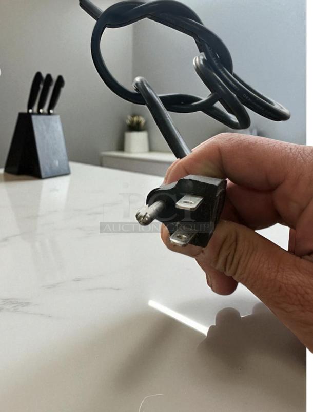 Black power plug held in hand, highlighting the 120V compatibility of the Curtis ALP3GTR12A000 coffee brewer.