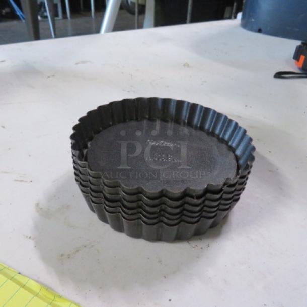 Wilton 4x1 inch mini tart/quiche pans, stack of 6, black non-stick, fluted edges, used condition with visible brand marking.