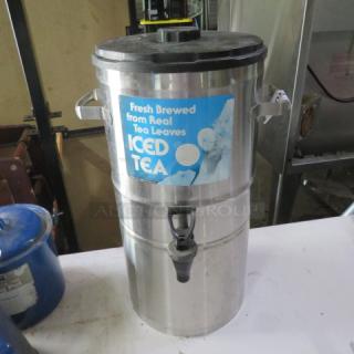 Stainless steel iced tea dispenser with spout, labeled "Fresh Brewed from Real Tea Leaves," in good condition.