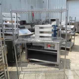 Metro three-shelf wire shelving unit, 48x18x73 inches, stainless steel, used condition. Industrial setting background.