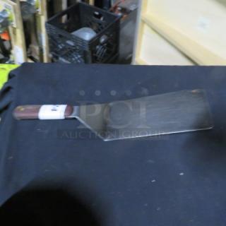 Metal hamburger turner with wooden handle, slight wear on blade, kitchenware accessory.